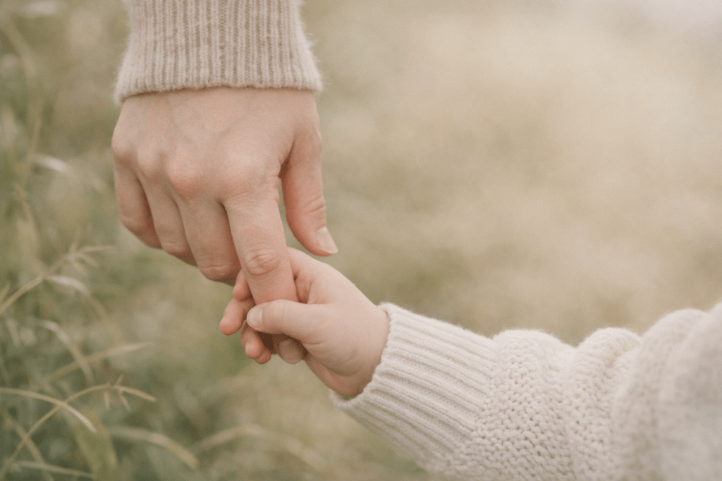 Adult hand gently holding a child’s hand outdoors.