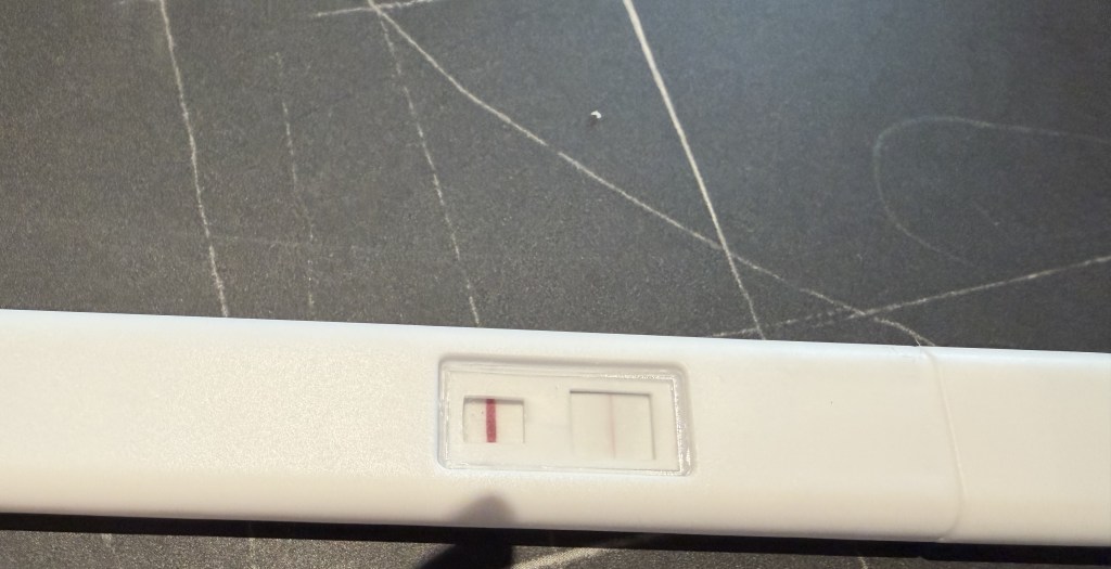 Positive pregnancy test showing two lines, one control line and one faint test line, on a dark scratched surface.